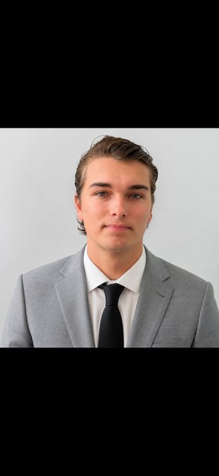 Professional headshot of a young man in a gray blazer, white shirt, and black tie against a neutral background