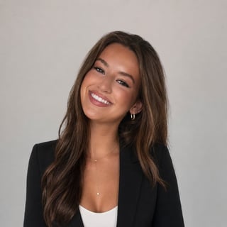 Smiling woman with long brown hair wearing a black blazer and white top against a gray background