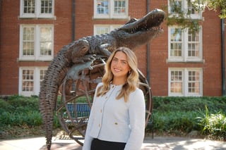 Woman smiling next to a large bronze alligator sculpture in front of a red brick building