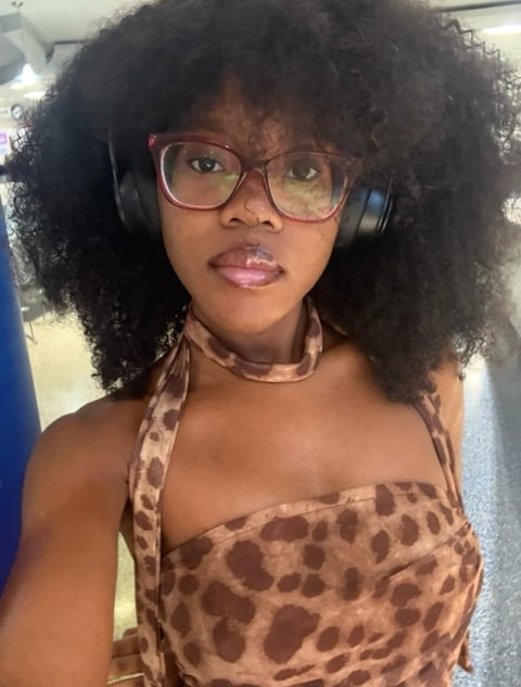 Person with curly hair wearing pink glasses, headphones, and leopard print halter top